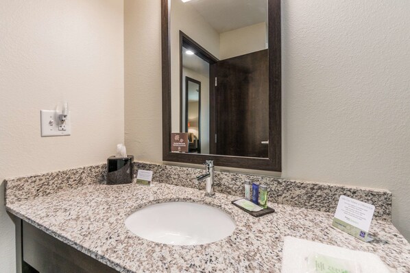 A hotel bathroom with a granite countertop, a white sink, a mirror, and a towel rack.