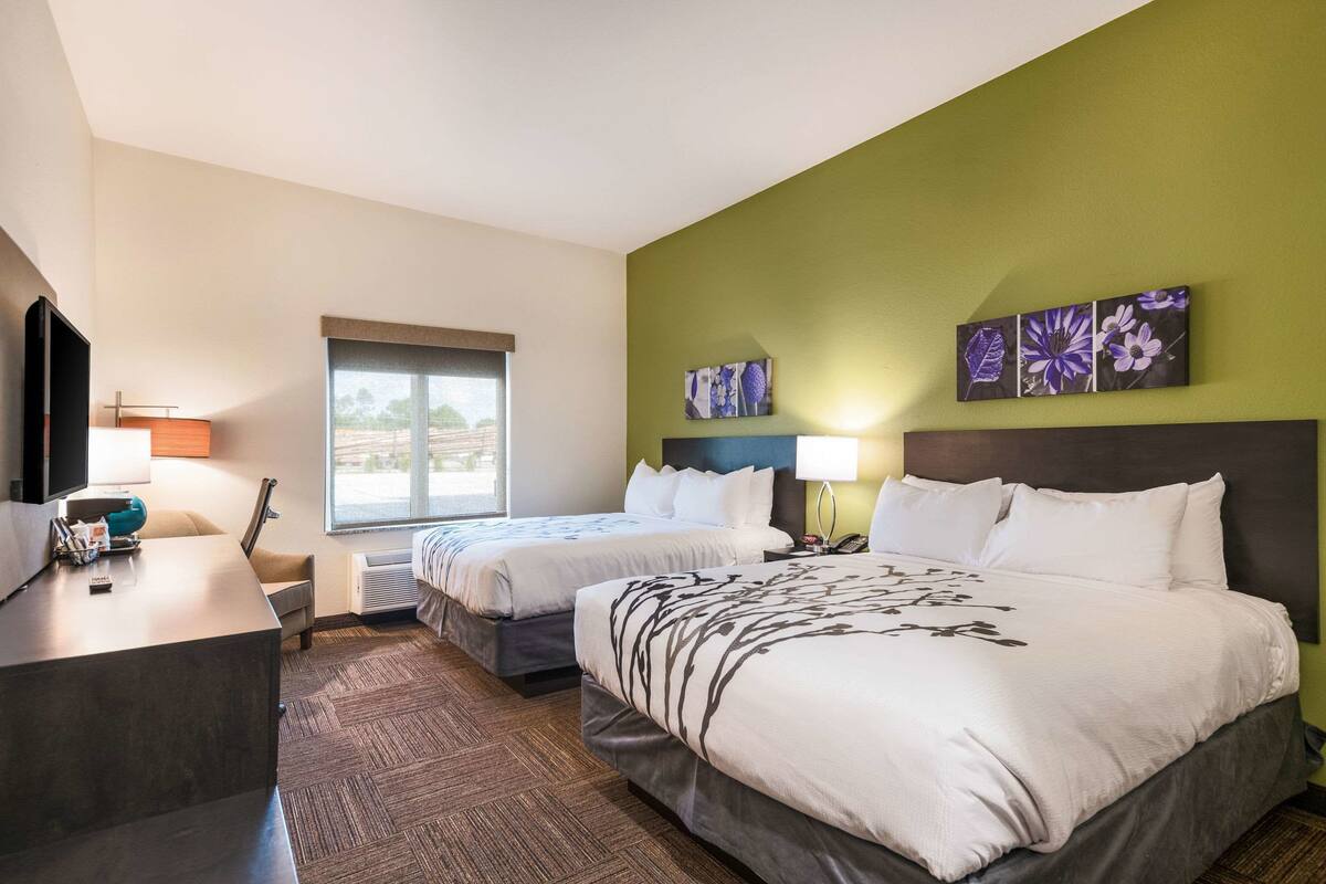 Ein Hotelzimmer mit zwei Betten, einem Schreibtisch, einem Fernseher und Bildern an der Wand.
