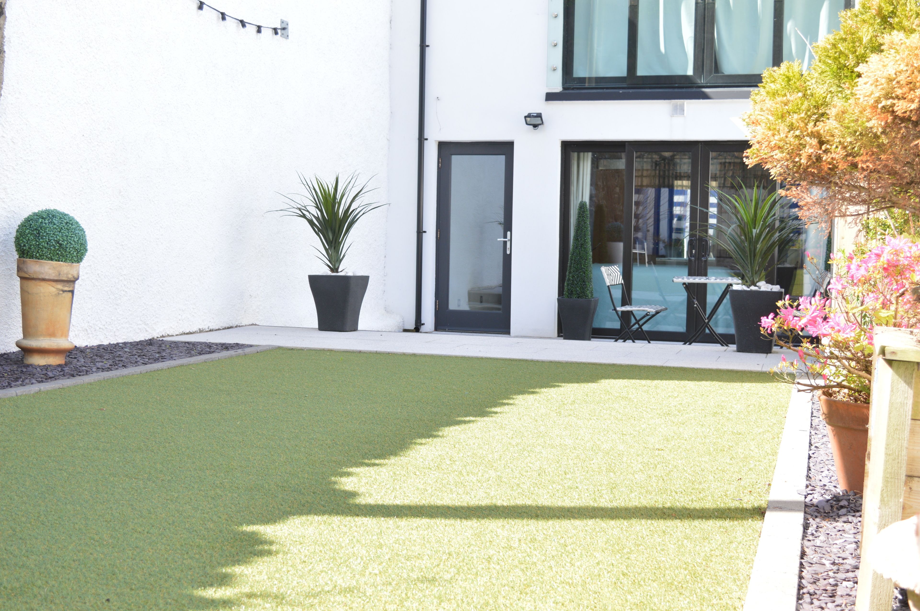 A courtyard with artificial grass, potted plants, and a seating area with tables and chairs.