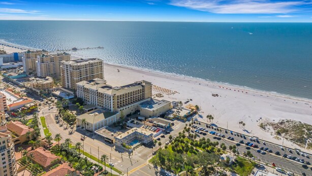 A coastal hotel with multiple buildings, a beach, and a parking area.