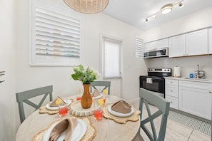 Una cocina moderna con armarios blancos, microondas, horno y una zona de comedor con mesa redonda, sillas y un jarrón con flores.