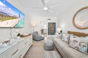 Een moderne woonkamer met een flatscreen televisie, een plafondventilator en een grote spiegel.