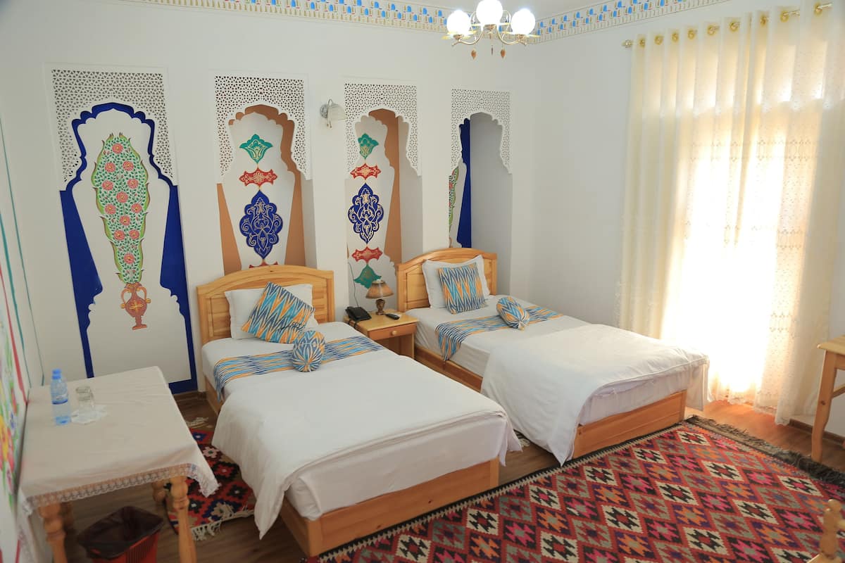 A room with two beds, a small table, and a patterned rug.