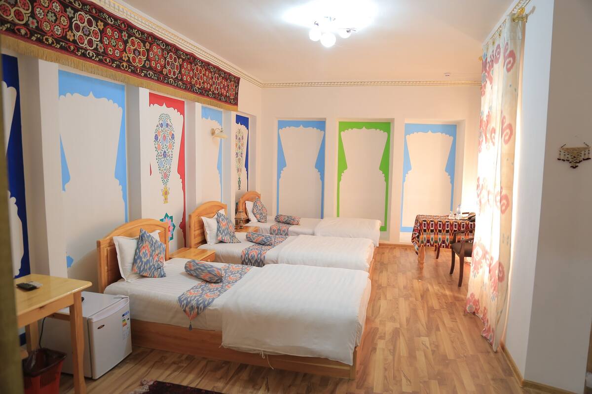 A hotel room with two beds, a small table, a desk, and a refrigerator.