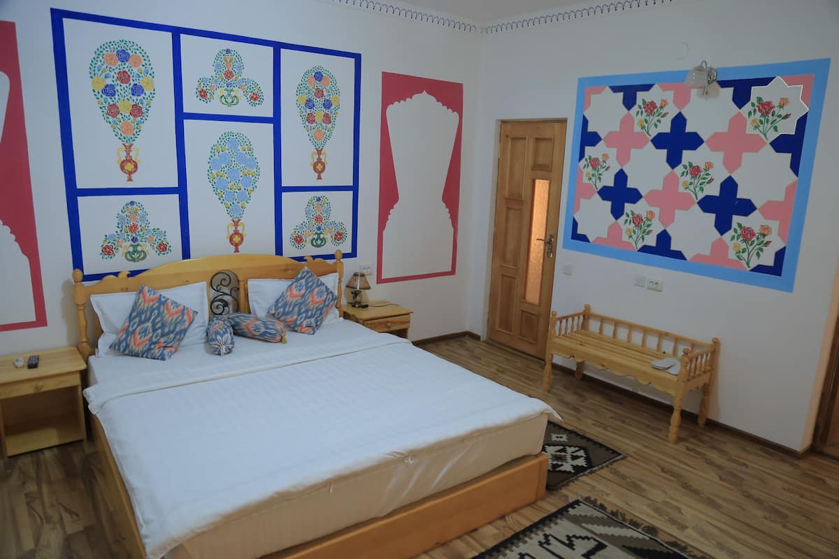 A bedroom with a wooden bed, a wooden bench, and a wall decorated with colorful artwork.