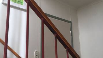 A staircase with a wooden handrail and red vertical supports, leading to a door with a number plate.
