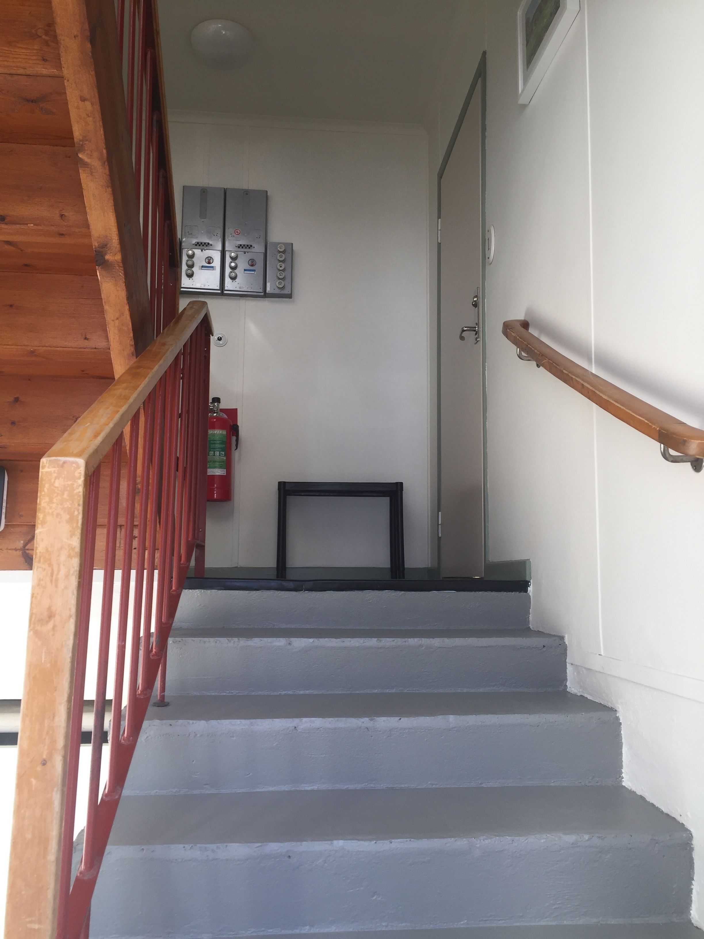 A staircase with wooden railings, a fire extinguisher, and a wall-mounted electrical panel.