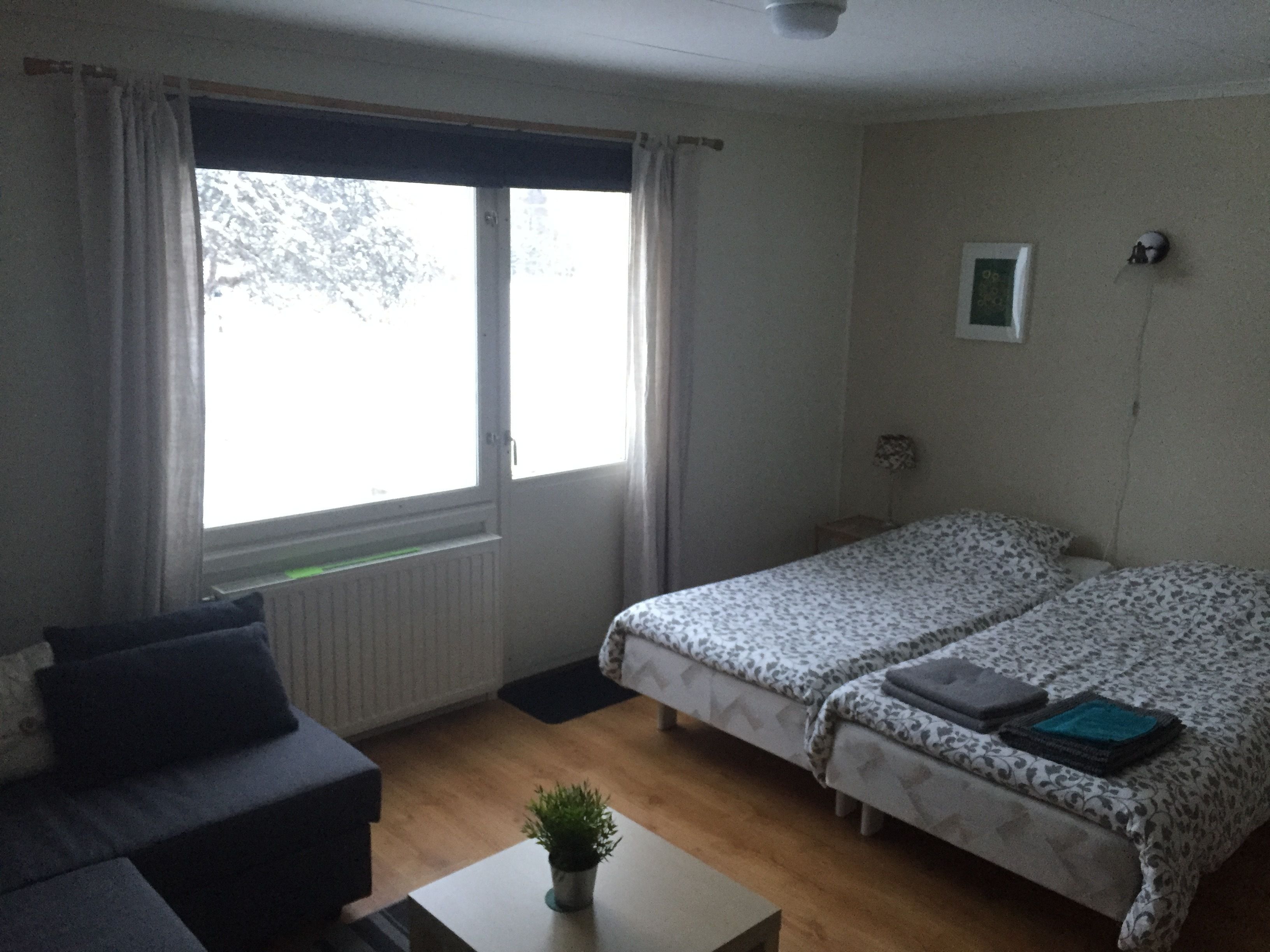 A room with a bed, a small table, a plant, and a window with curtains.