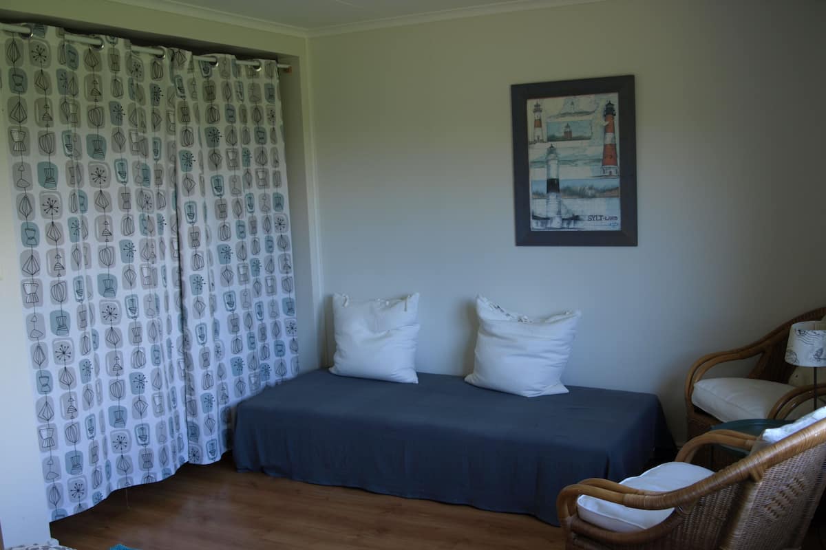 A room with a bed, two pillows, a chair, a lamp, and a painting on the wall.