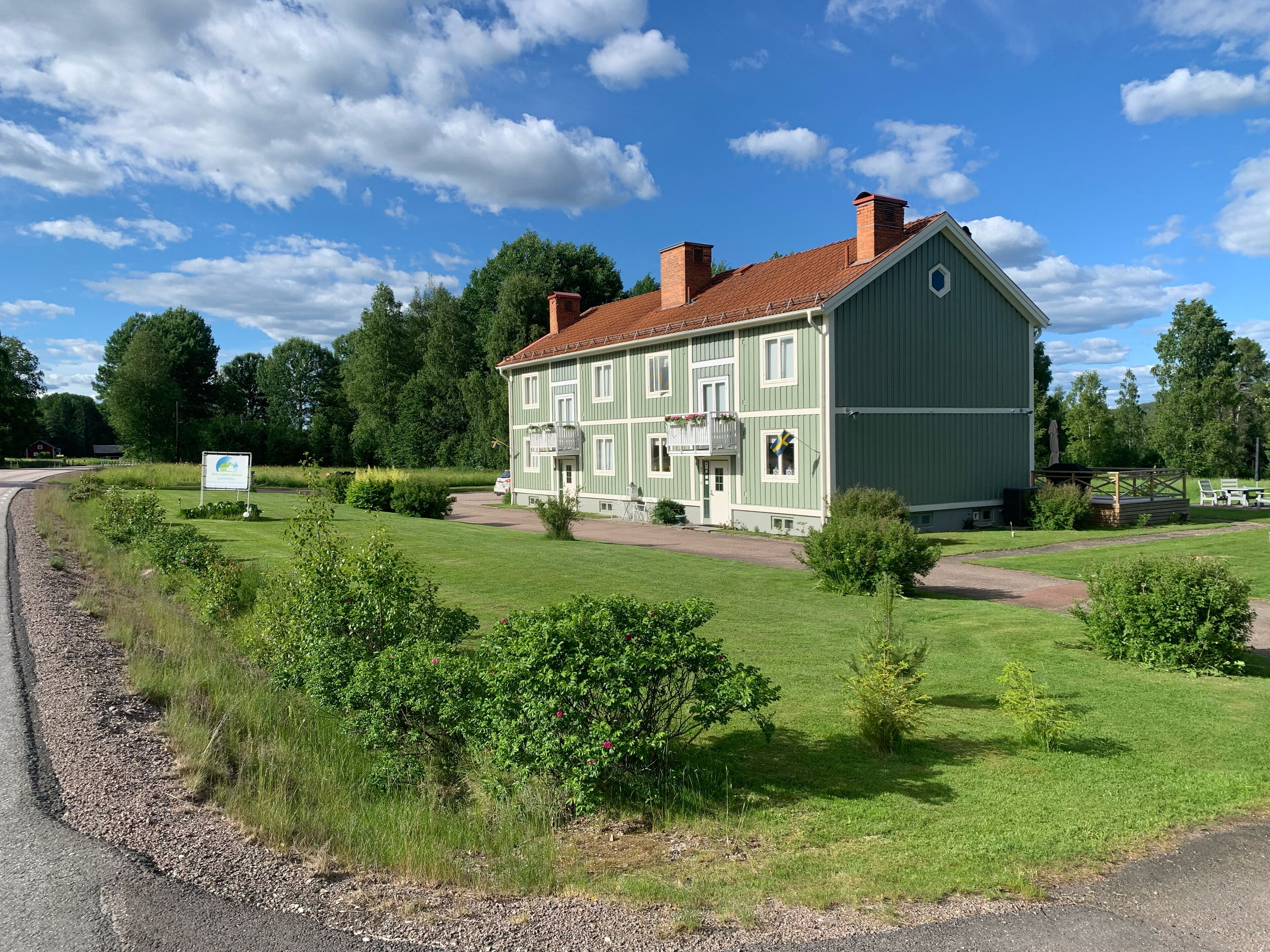 Un grand bâtiment à deux étages, doté d’une façade verte et d’un toit recouvert de tuiles rouges, entouré d’une pelouse bien entretenue et d’arbres.