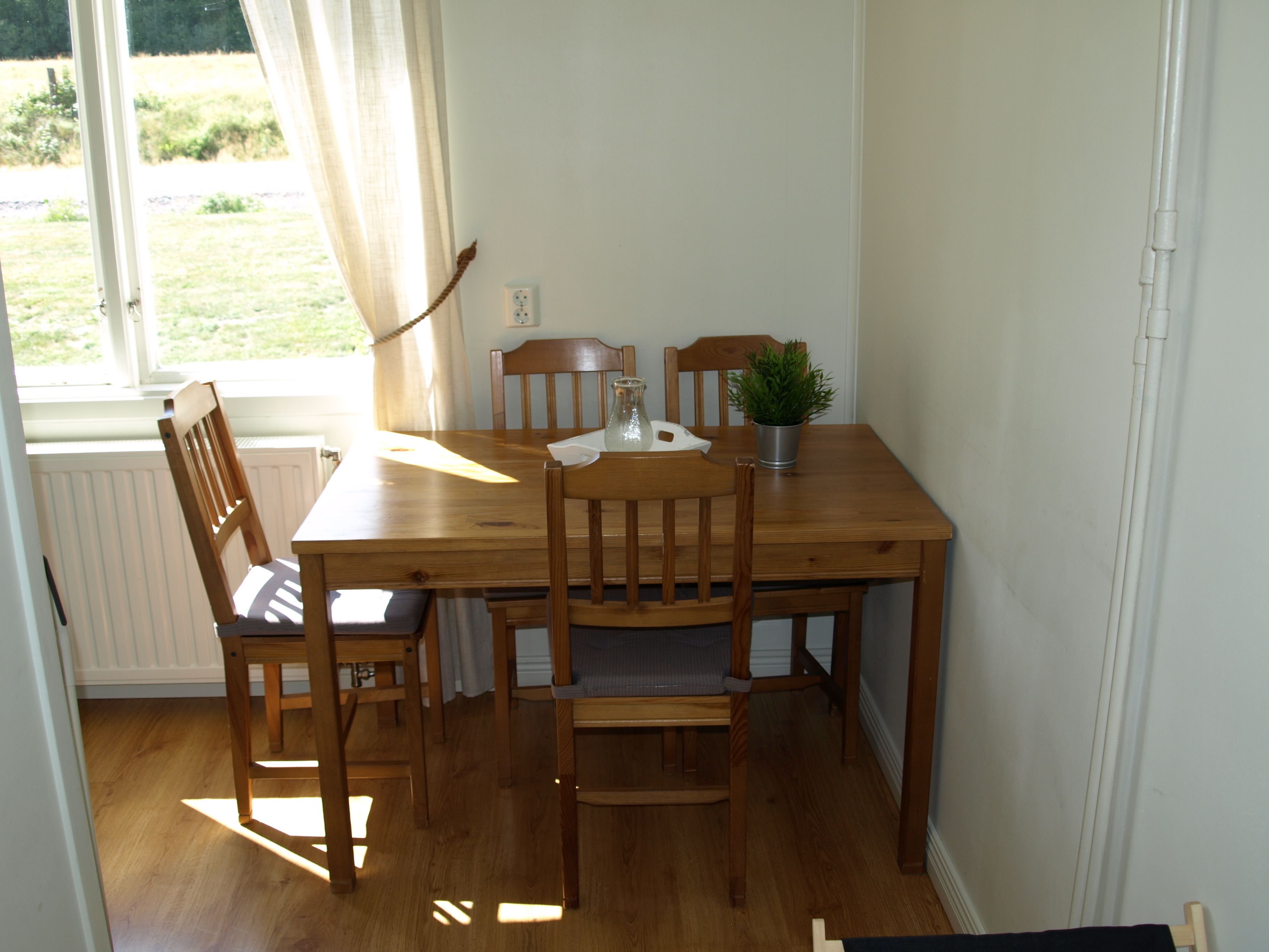 A dining area with a wooden table and chairs, a potted plant, and a window with curtains.