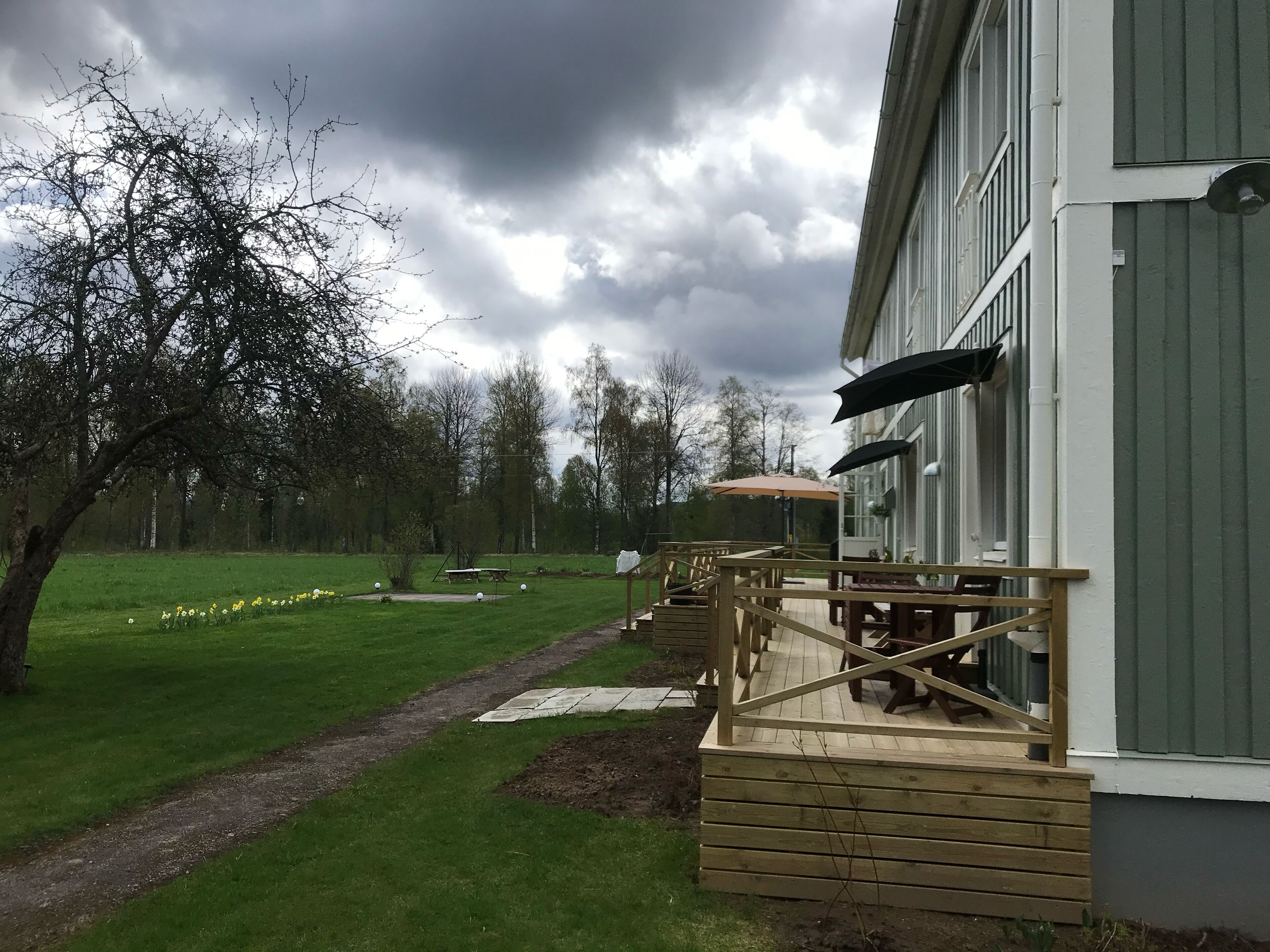 A wooden deck with outdoor seating, a pathway, and a grassy area with trees.