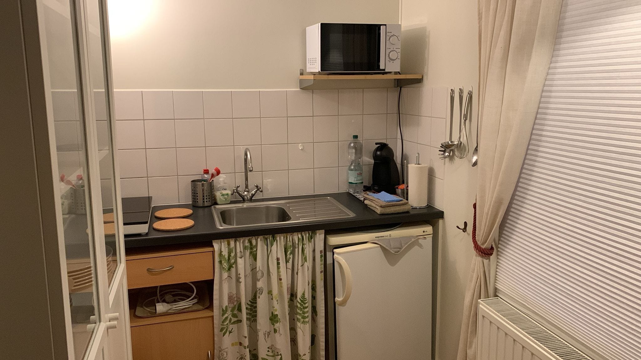 Una cucina compatta con microonde, lavandino e un piccolo piano di lavoro.