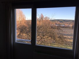 A room with two windows overlooking a landscape with trees and a body of water.