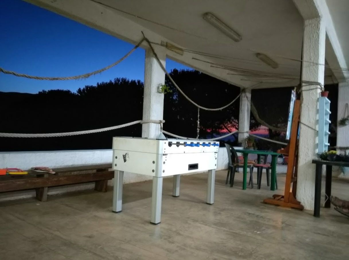 A foosball table in a covered outdoor area with a bench and tables.
