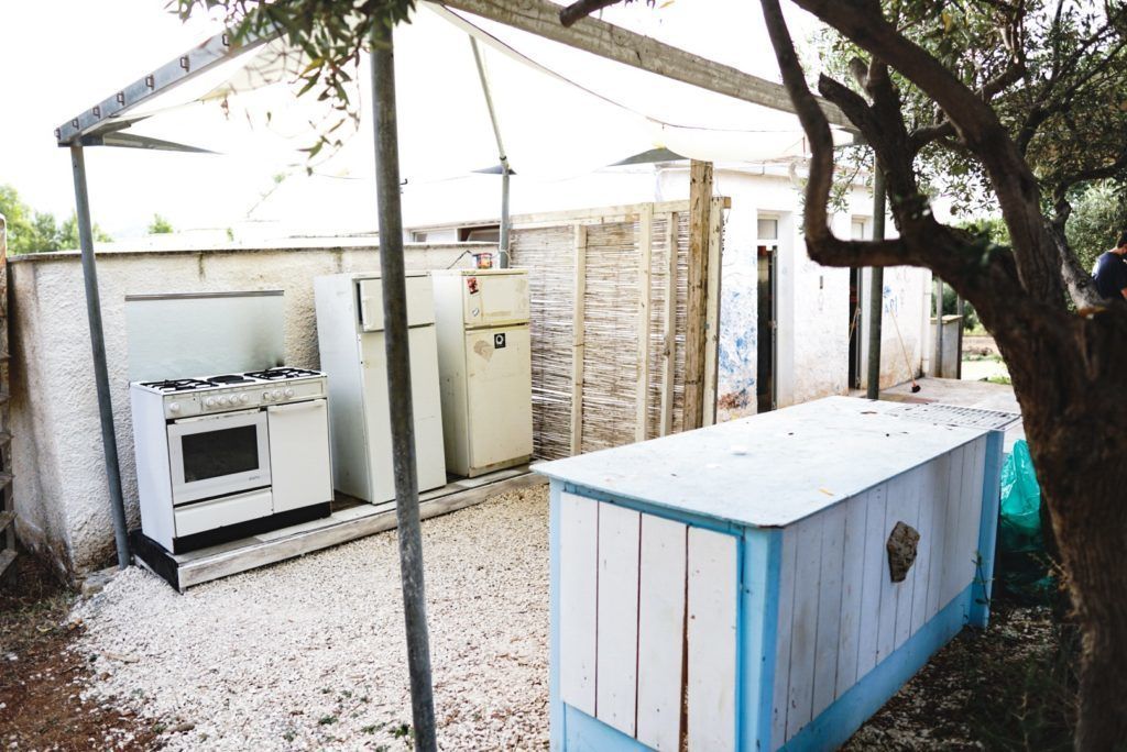 Patio trasero con estufa a gas, refrigerador y un cobertizo azul.