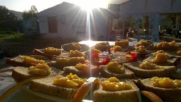 Una mesa con rebanadas de tostadas cubiertas de fruta, ubicada al aire libre con un edificio y árboles al fondo.