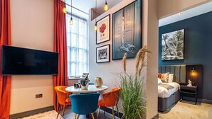 A modern living room with a flat-screen TV, a dining area with orange chairs, a large potted plant, and artwork on the walls. - Mrs Blodget's (Liverpool)