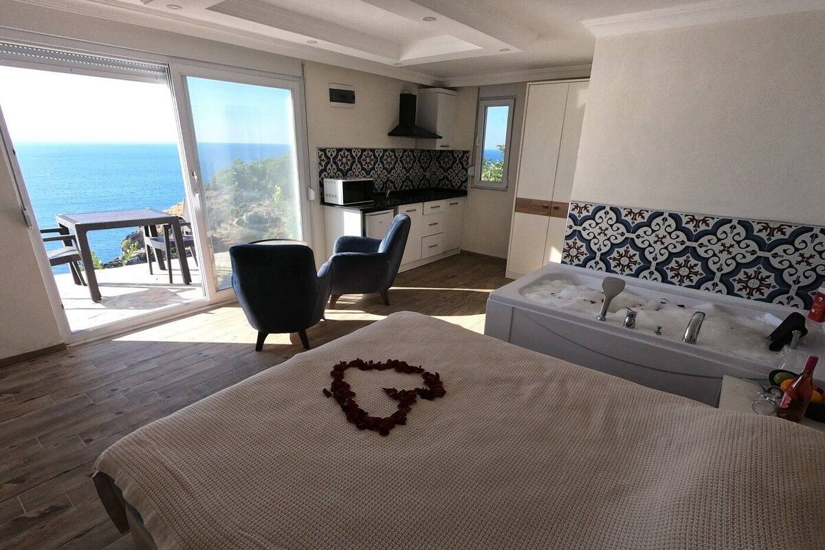 A bedroom with a large bed, a heart-shaped decoration, a bathtub, and a view of the sea.