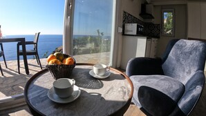 Una habitación con vista al mar, una mesa de comedor con una cesta de fruta, una silla y una zona de cocina con microondas.