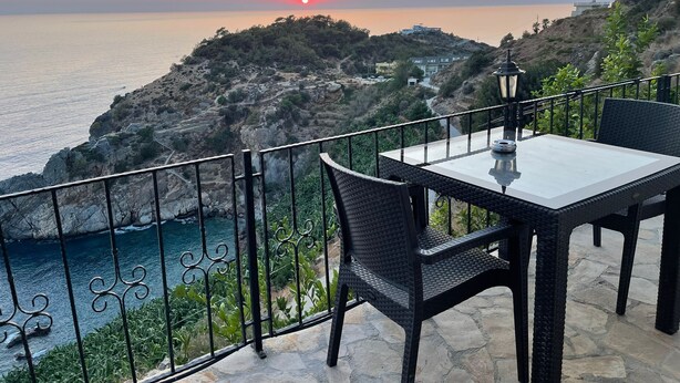Una mesa y sillas en un balcón con vistas a un paisaje costero al atardecer.