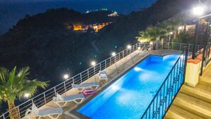 Piscina con sillas de descanso y barandilla, rodeada de palmeras y con vistas a una zona montañosa.
