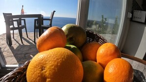 Una cesta de mimbre llena de naranjas y una manzana verde en un balcón con mesa y sillas, con vistas al mar.