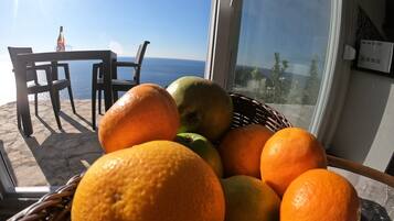 A wicker basket filled with oranges and a green apple on a balcony with a table and chairs, overlooking the sea.