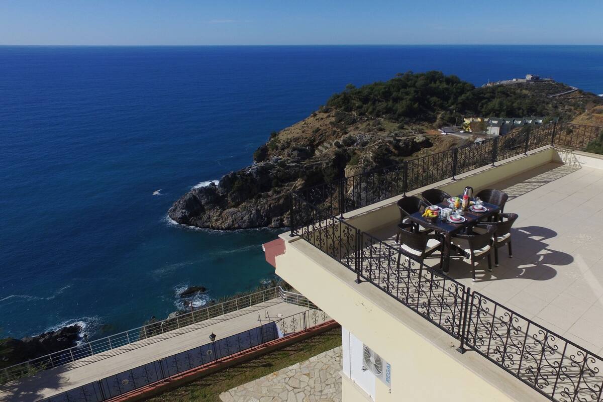 A terrace with a table set for dining, overlooking a rocky coastline and the sea.