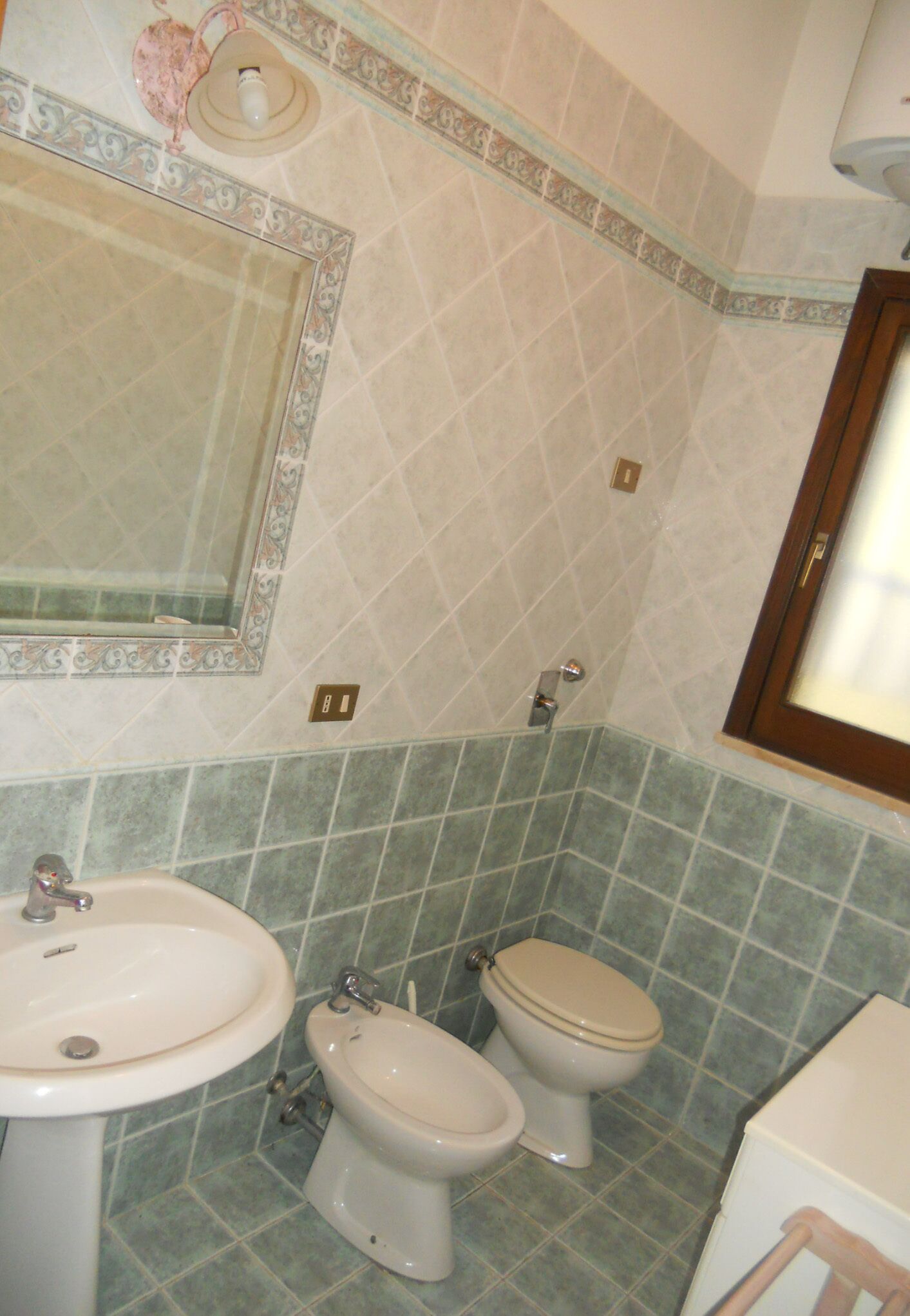 A bathroom with a sink, toilet, and bidet. The walls are tiled with a geometric pattern.
