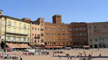 A spacious public square with historic buildings, a central fountain, and people gathered around.