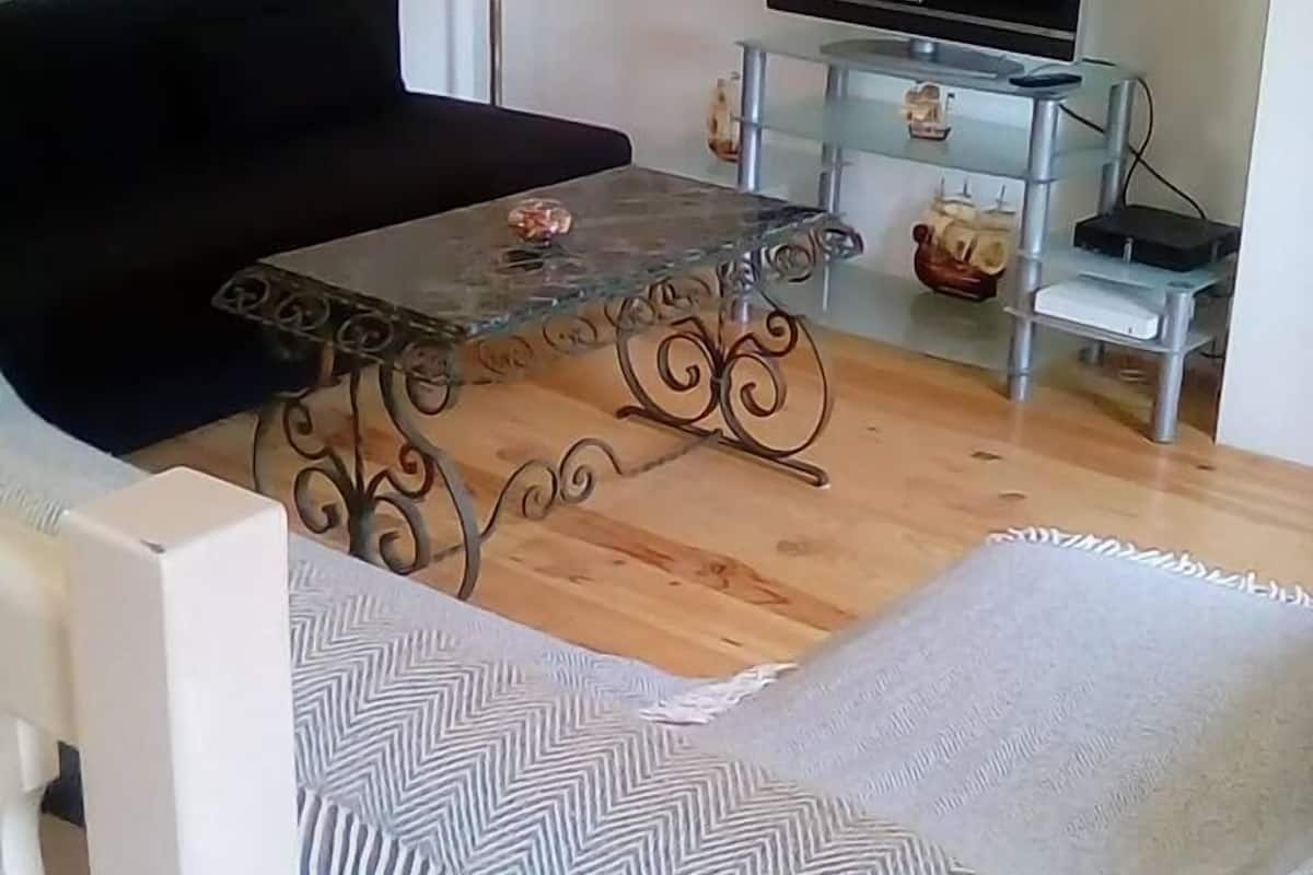 A living room with a black sofa, a glass coffee table with metal legs, a television on a stand, and a patterned rug.