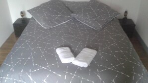 A neatly made bed with a grey patterned bedspread, two pillows, and two folded towels on the bed. - Le Trois Mâts (Thiers)