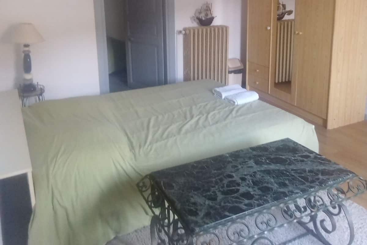 A bedroom with a bed, a wooden wardrobe, a radiator, and a small table.