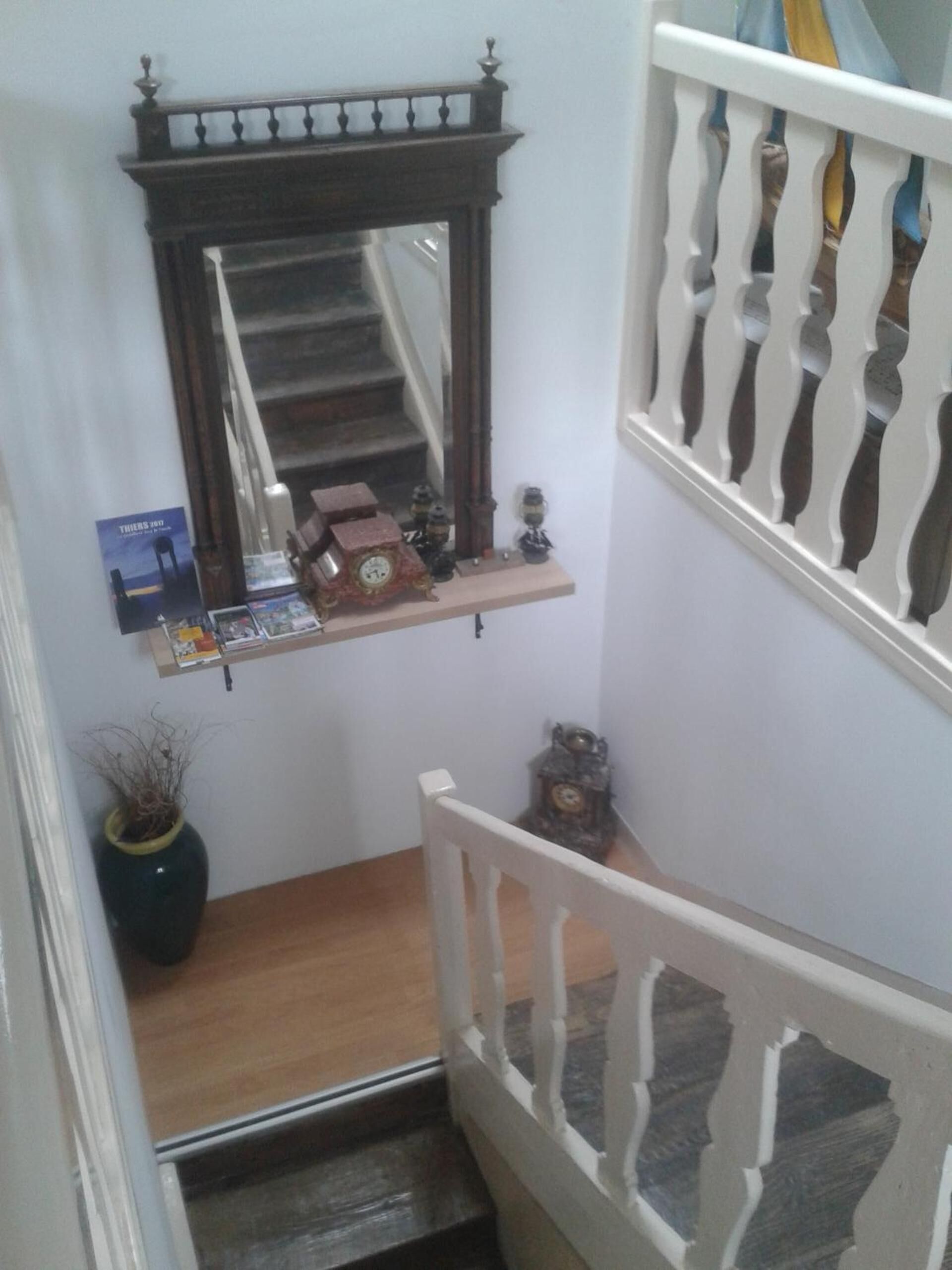 Una escalera con baranda blanca, un estante de madera con un reloj y una pequeña planta en maceta.