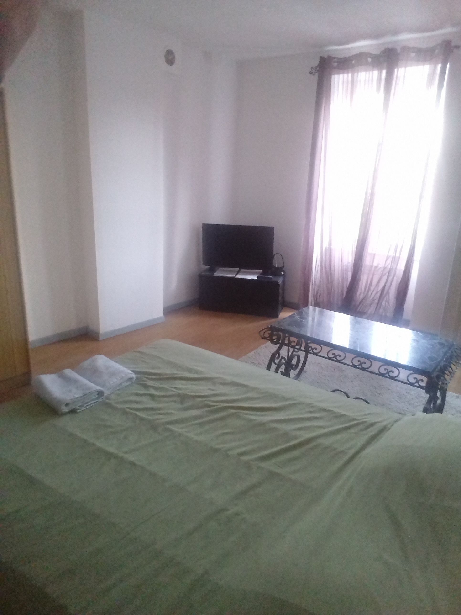 Une chambre avec un lit, une petite table, un téléviseur et une fenêtre avec des rideaux.