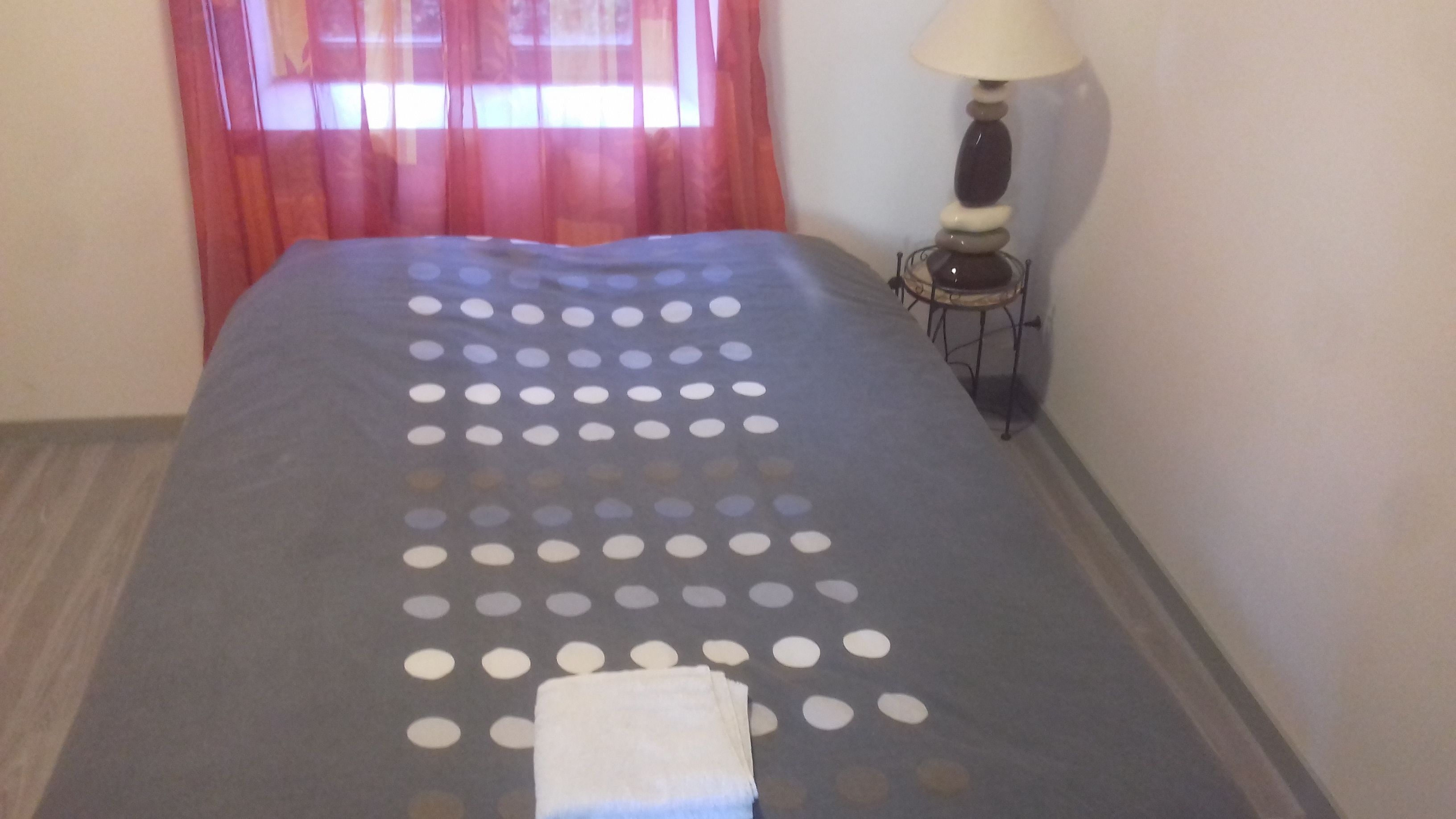 Un lit bien fait, avec une couvre-lit à pois et une serviette blanche pliée au pied du lit.