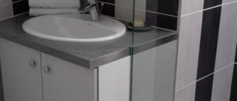 Un baño moderno con un lavamanos blanco, una cabina de ducha con mampara de vidrio y paredes con azulejos blanco y negro.