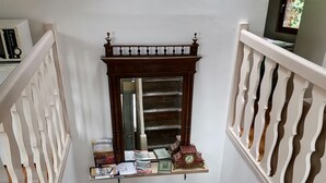 A staircase with a wooden handrail and white balusters, leading to a landing with a small shelf displaying books and a clock. - Le Trois Mâts (Thiers)
