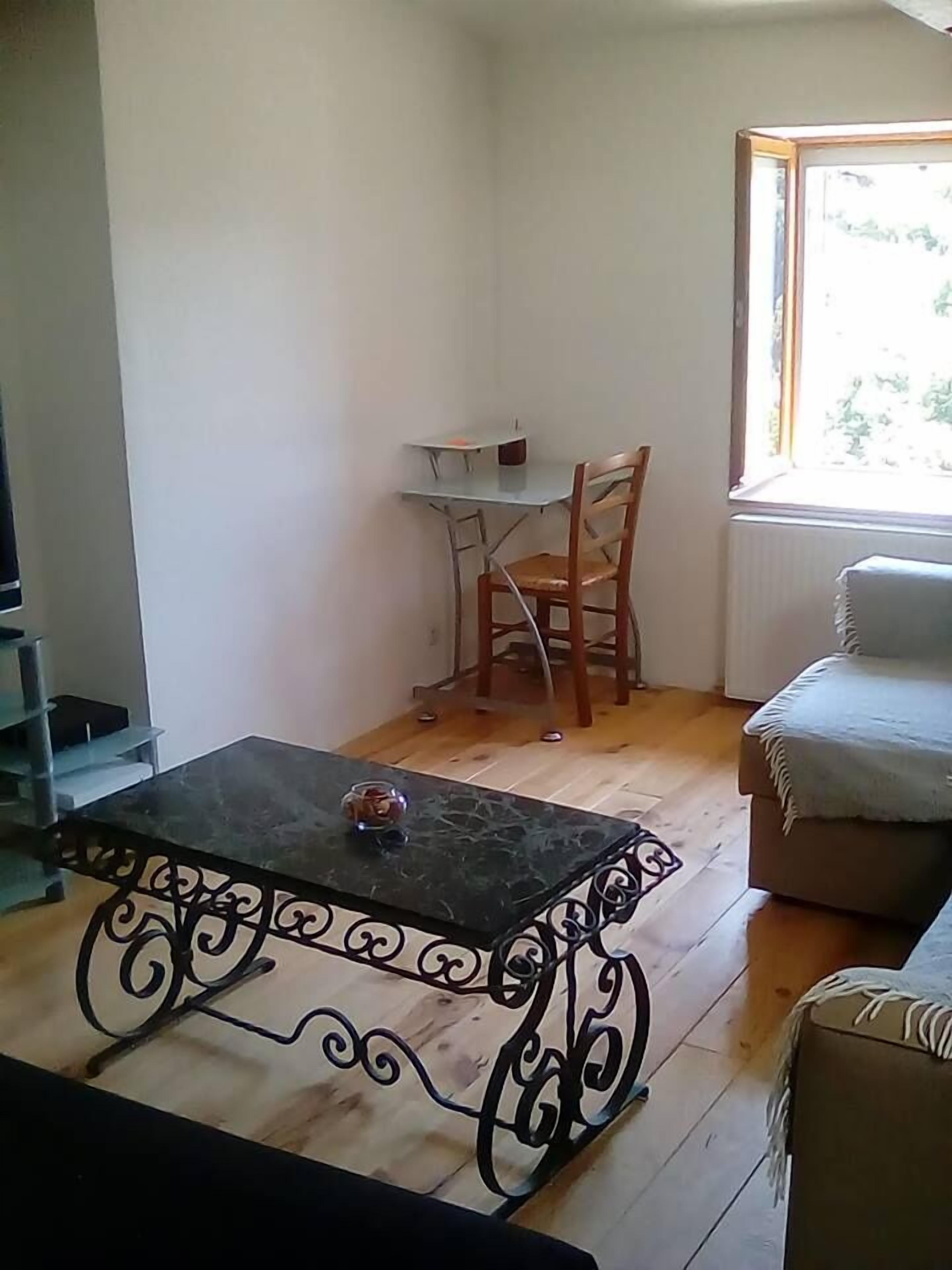 A living room with a wooden floor, a black metal coffee table, a white sofa, and a small table with a chair.