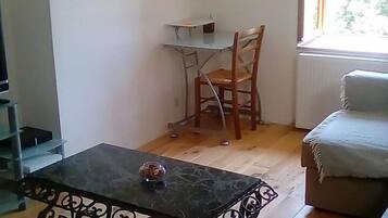 A living room with a wooden floor, a black metal coffee table, a white sofa, and a small table with a chair.