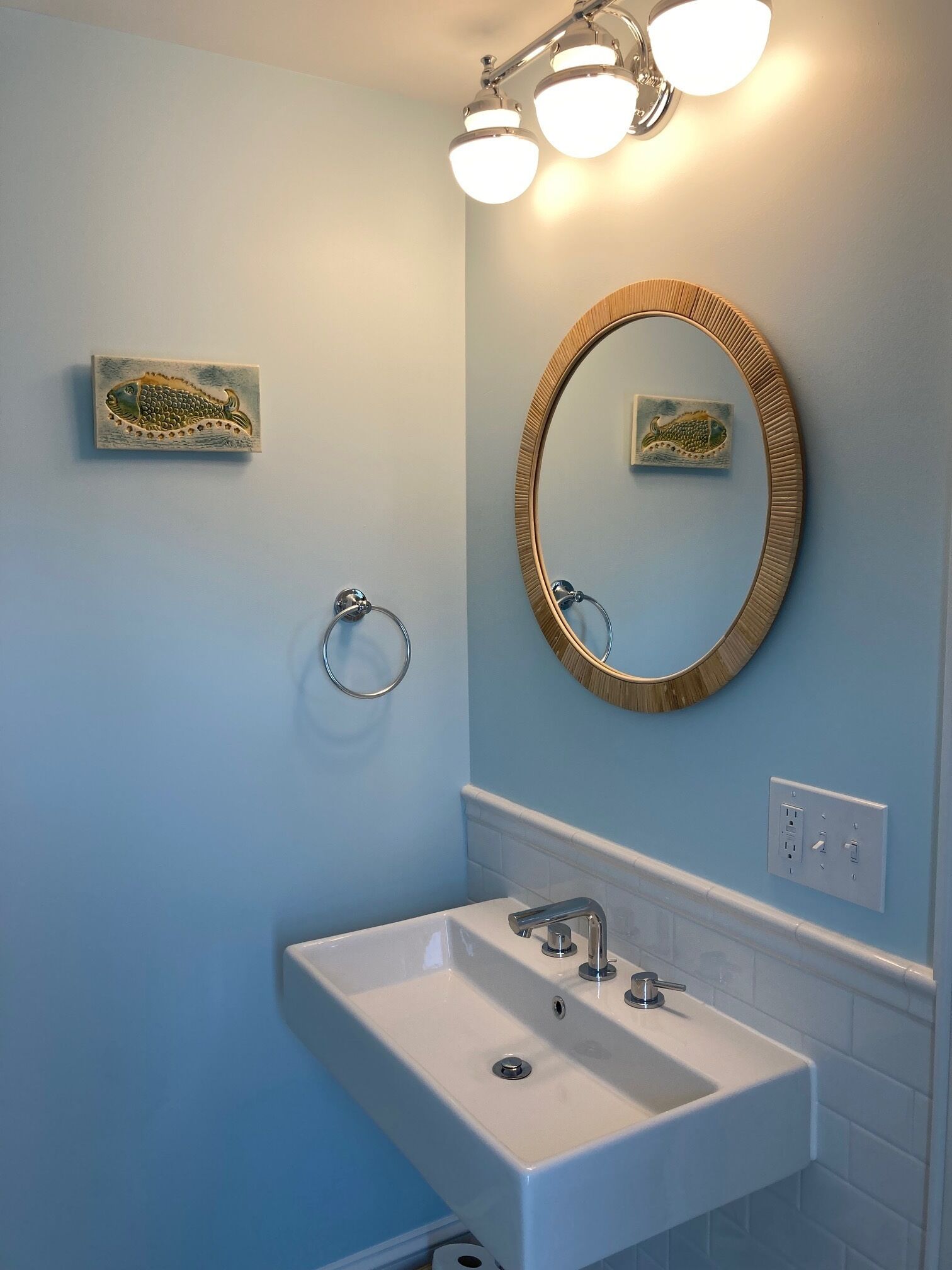 A bathroom with a white sink, a round mirror with a gold frame, and a wall-mounted light fixture.
