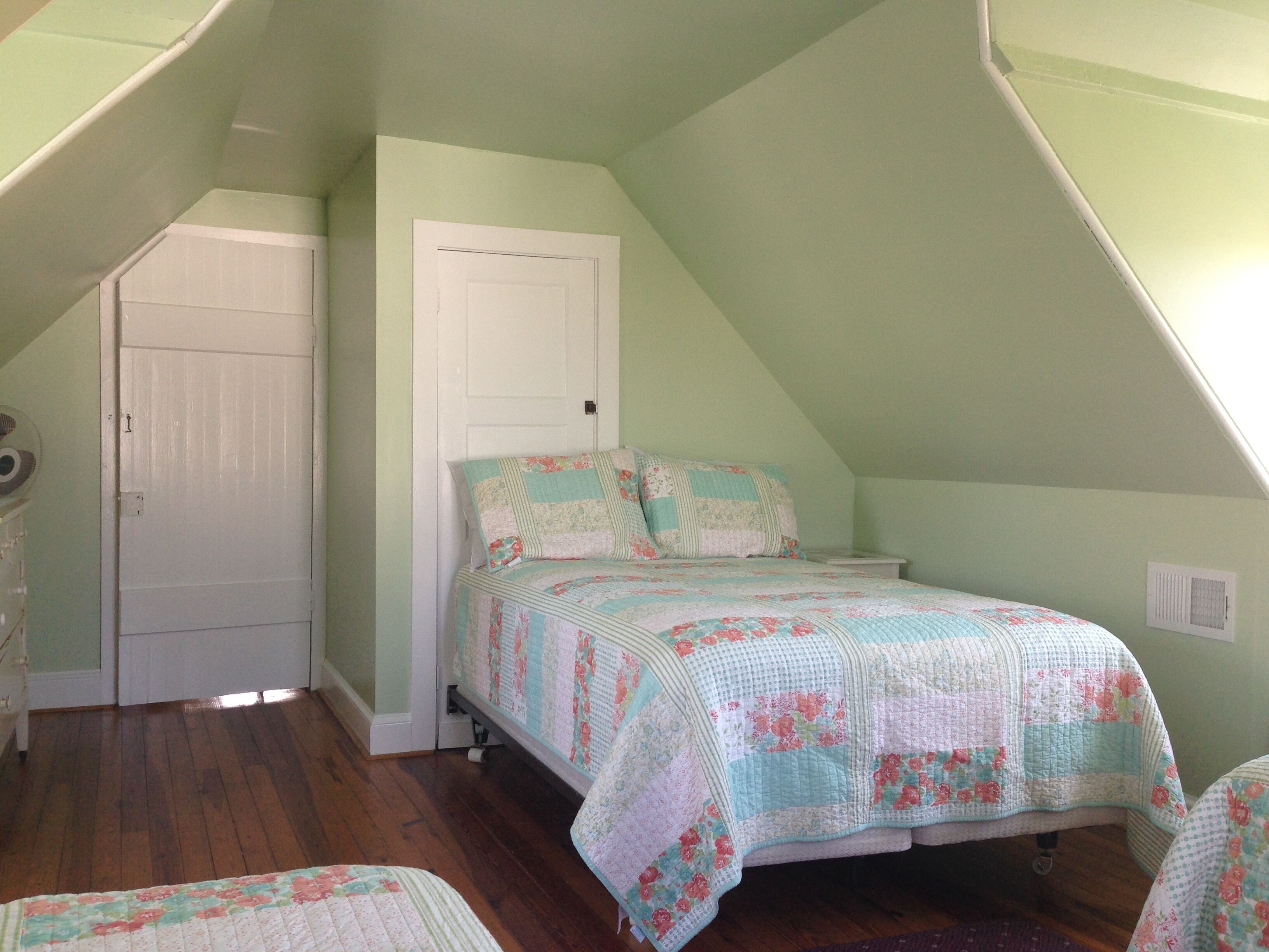 A small, cozy attic bedroom with a sloped ceiling, a single bed with floral bedding, a white door, and a wooden floor.