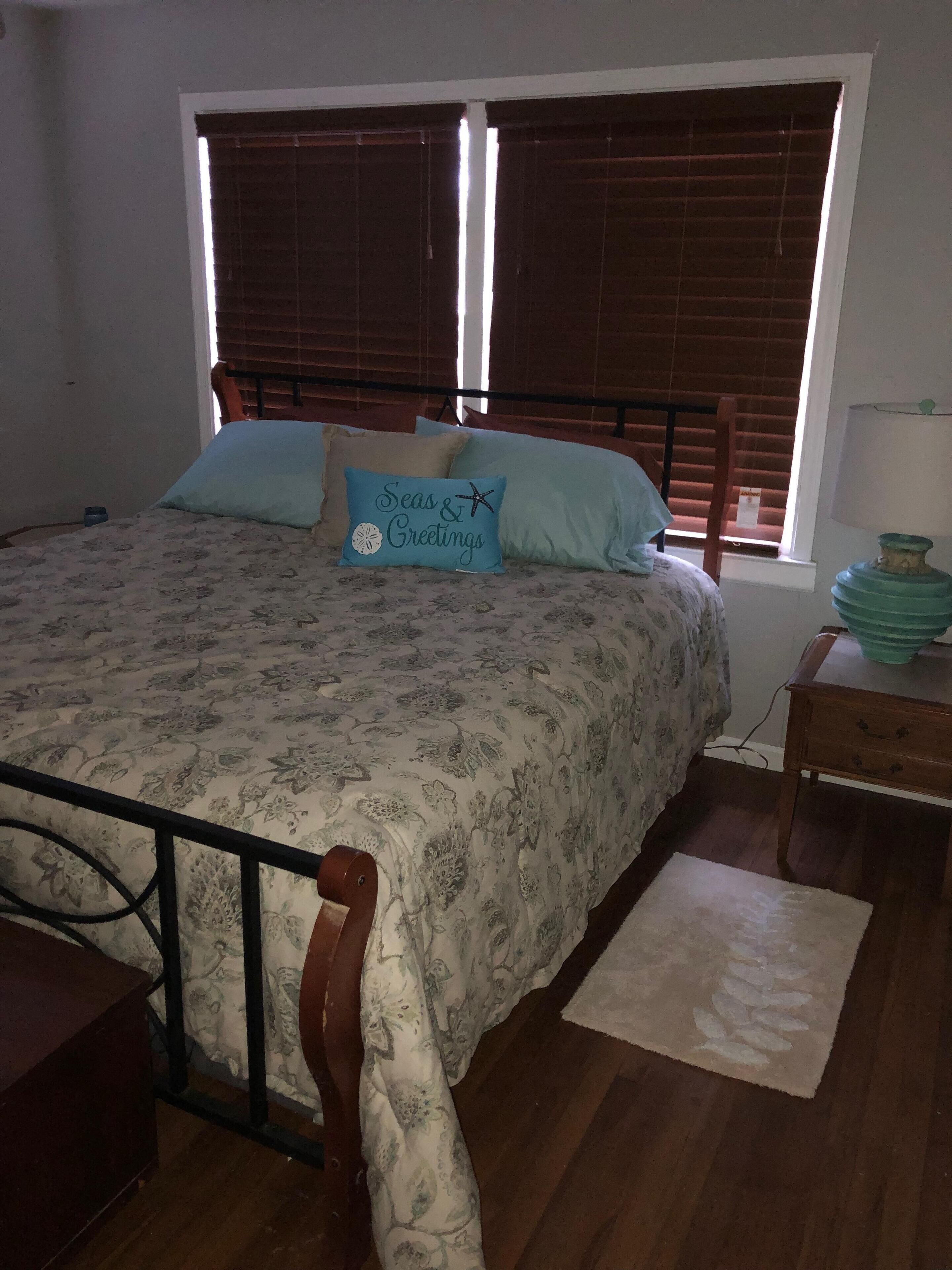 Una camera da letto con un letto, una testiera in legno, una finestra con persiane, un comodino e un tavolino.