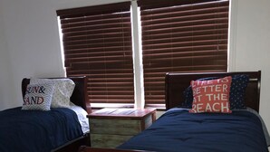 A bedroom with two wooden beds, a wooden nightstand, and a window with blinds. - Relax in Galveston, Texas! (Galveston)