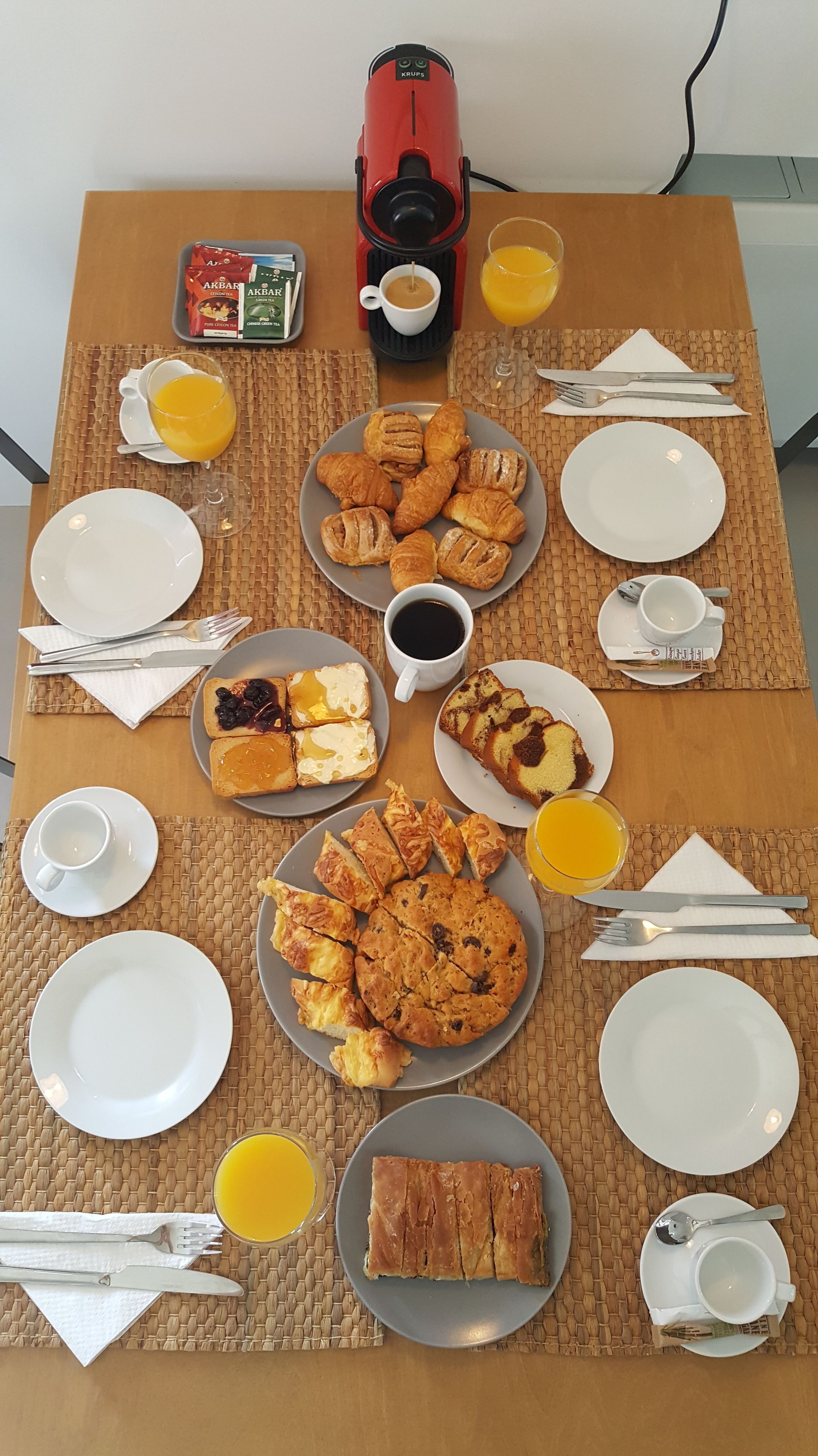 A breakfast table with various food items, a coffee maker, and a glass of orange juice.