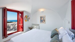 A bedroom with a large bed, a view of the sea through an open window, and a red door. - Aplada Suites (Santorini)