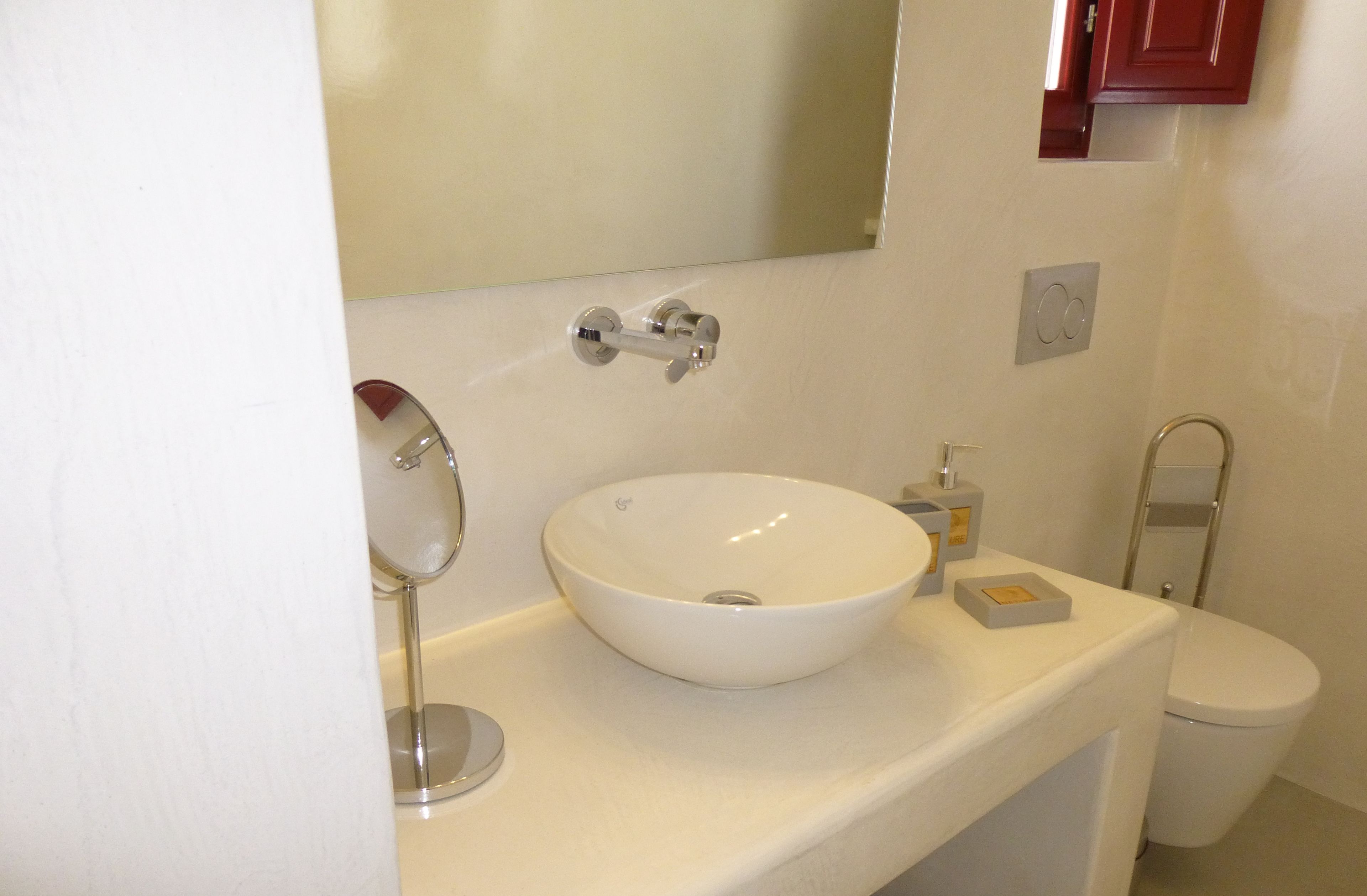 A bathroom with a white sink, a mirror, a toilet, and a red cabinet.