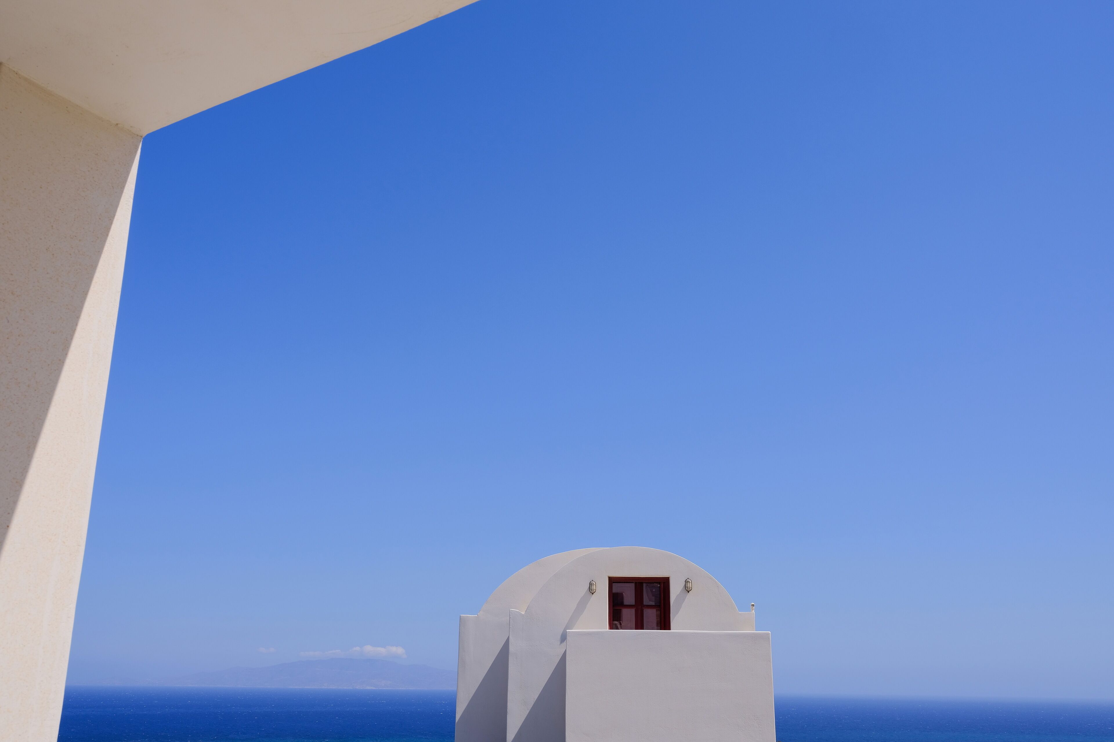 Un edificio blanco con una ventana pequeña, frente a un cielo azul despejado y vista al océano.