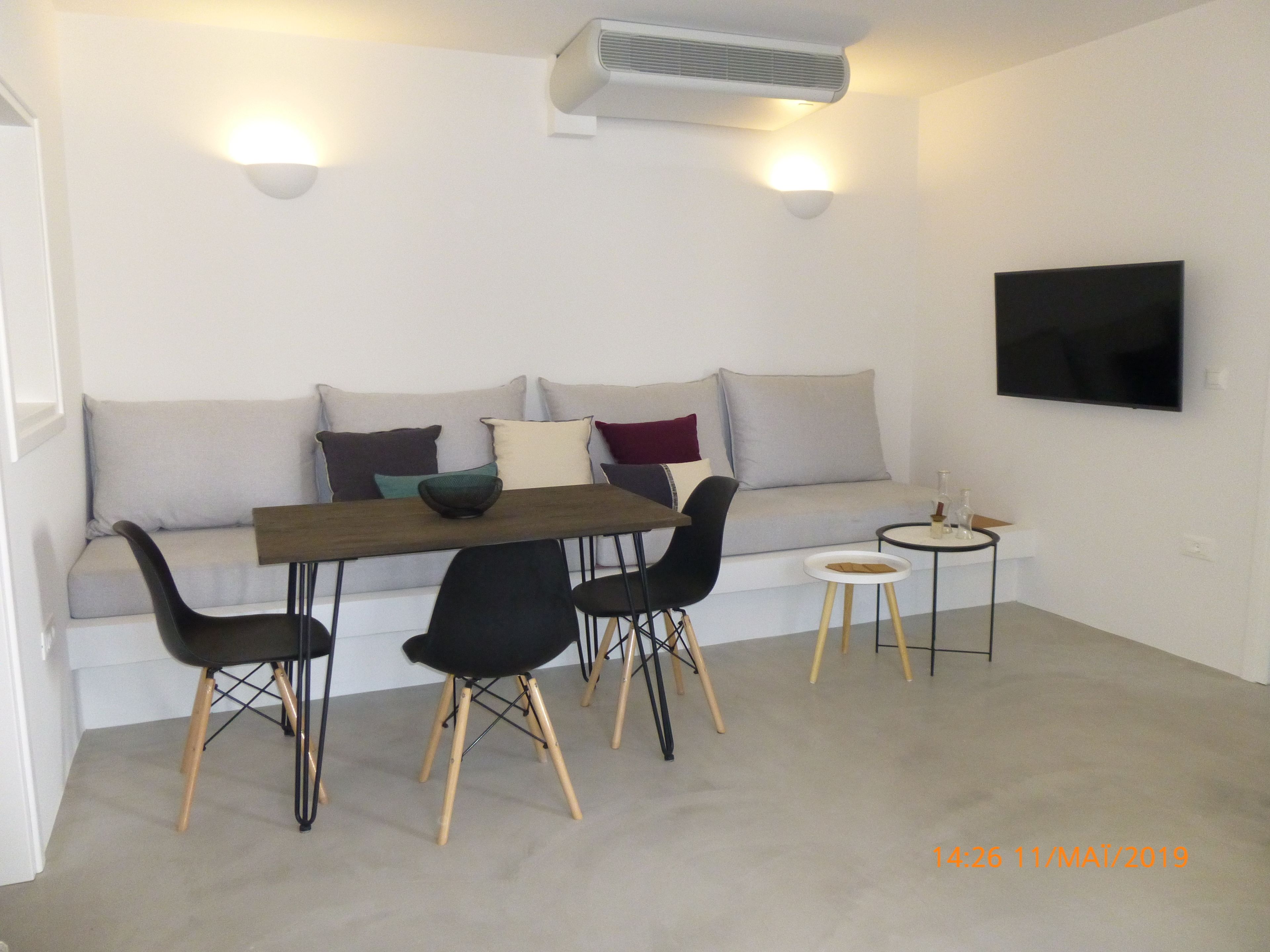 Una sala moderna con un sofá, una mesa de comedor y sillas. También hay una mesita auxiliar y un televisor de pantalla plana montado en la pared.